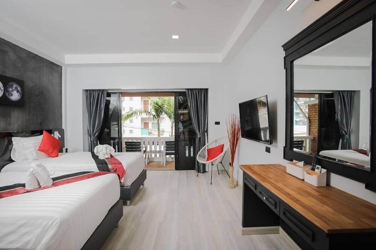 Habitación de hotel moderna con dos camas, un televisor, un escritorio y un balcón con vistas a edificios.