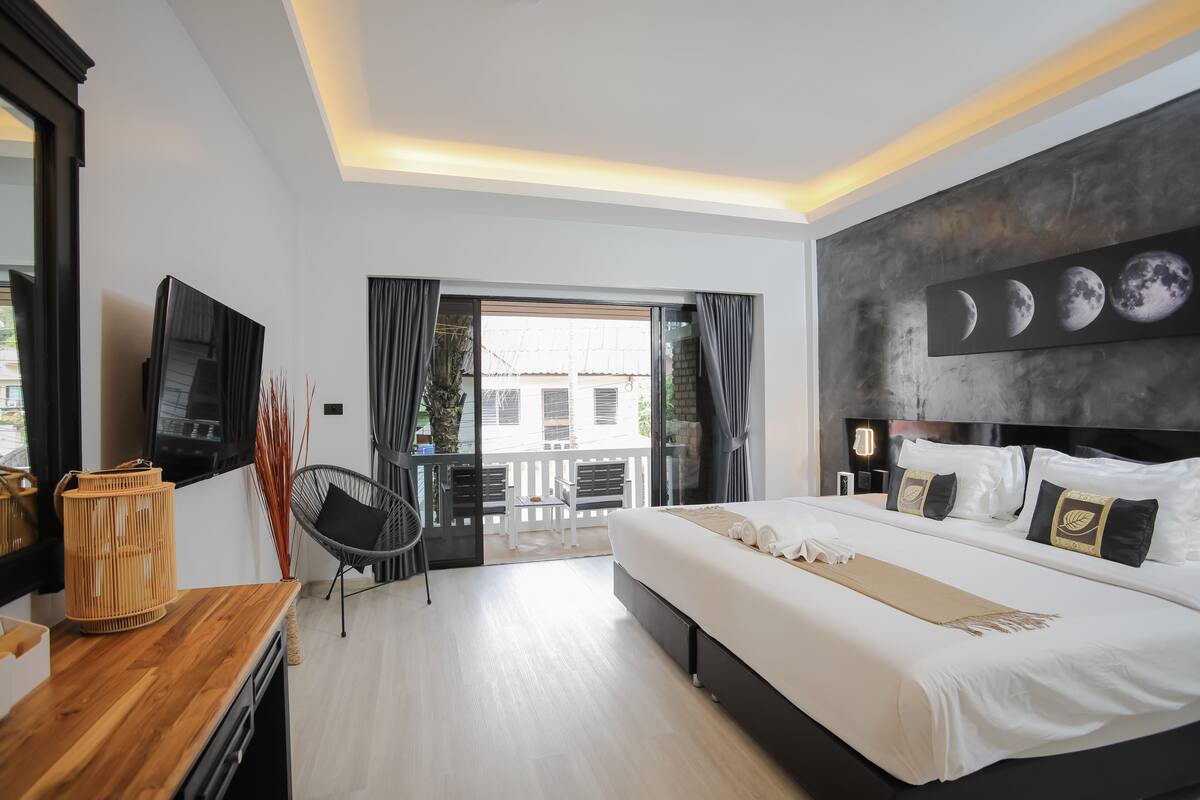 Una habitación de hotel moderna con una cama grande, un televisor de pantalla plana, un escritorio de madera y un balcón con vistas a la ciudad.
