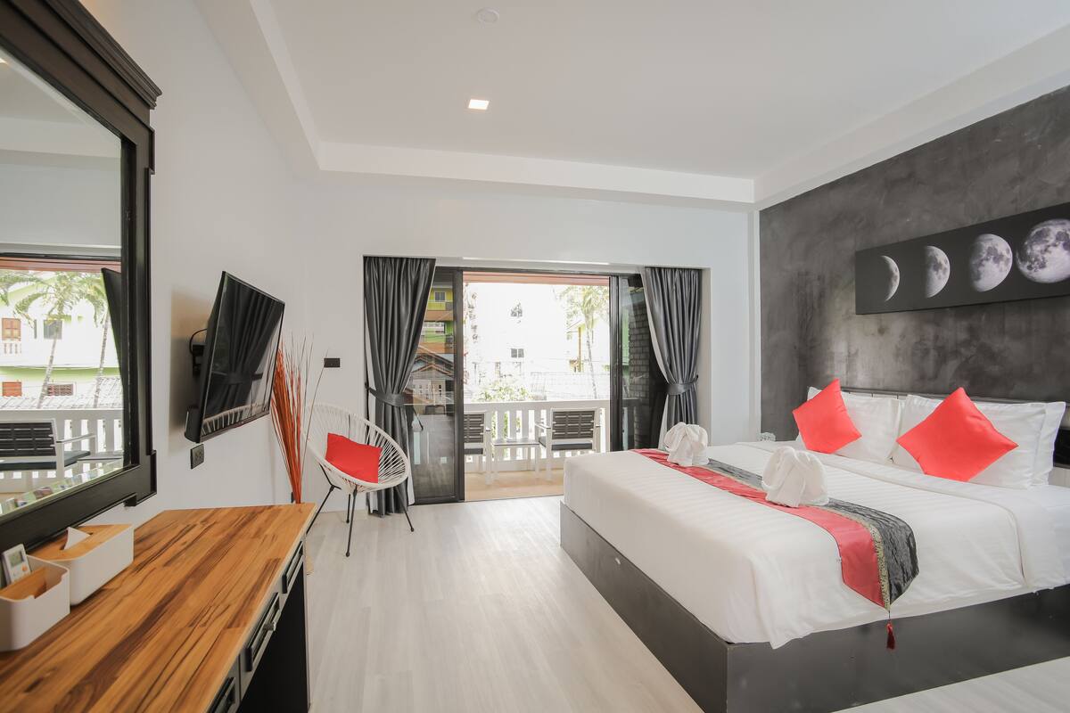 Habitación de hotel moderna con una cama grande, un escritorio con silla, televisión y un balcón con vistas al exterior.