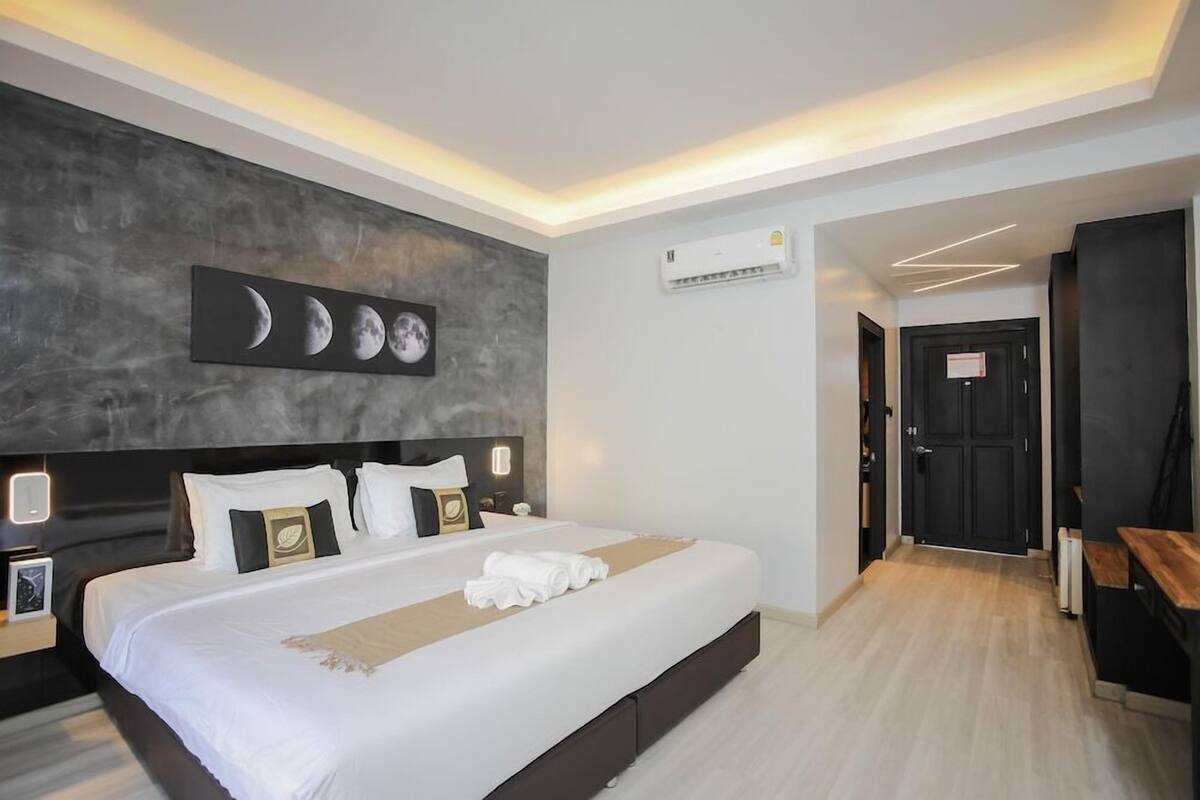 Una habitación de hotel moderna con una cama grande, una obra de arte con las fases de la luna en la pared, un equipo de aire acondicionado y piso de madera.