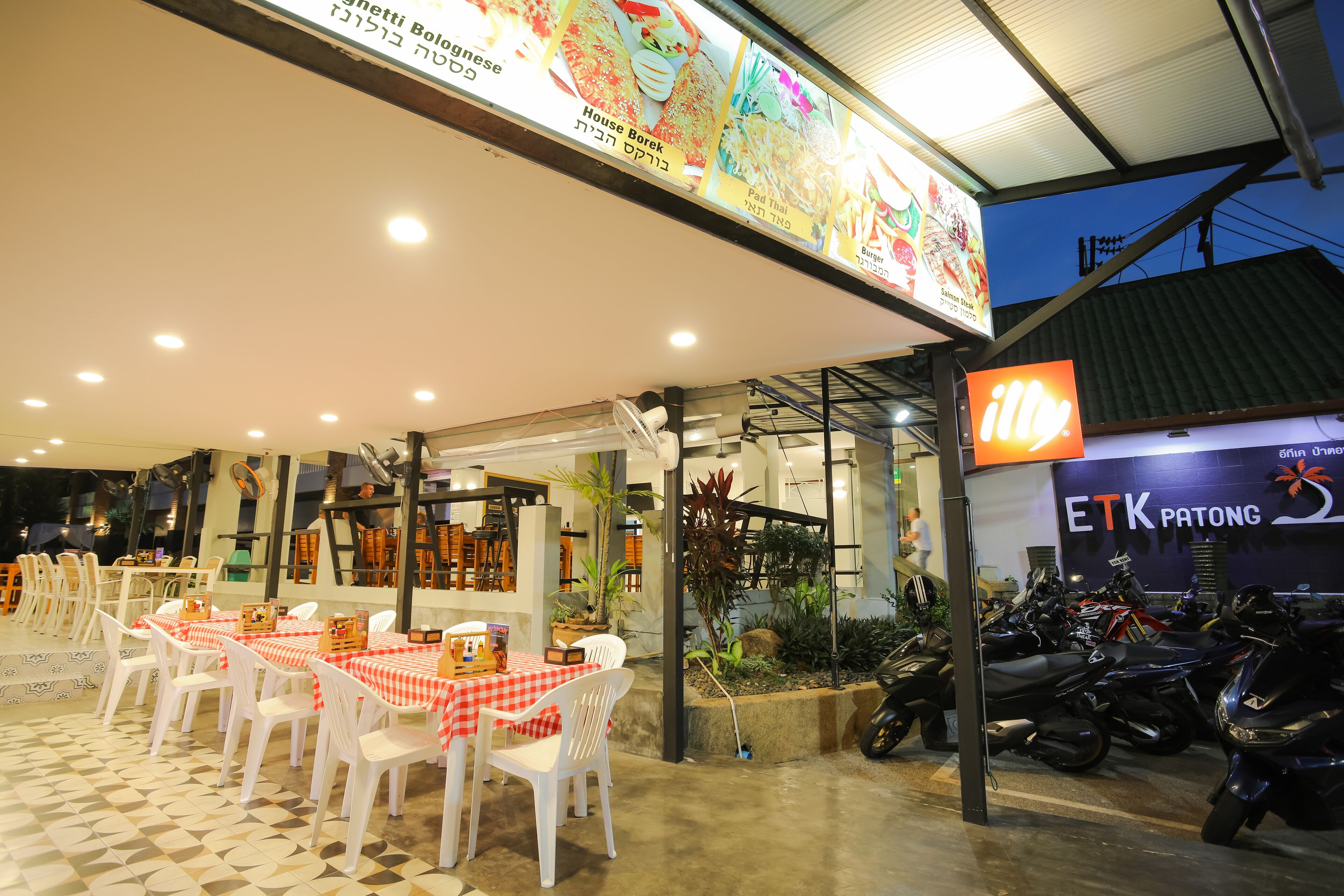 An outdoor dining area with tables and chairs, a menu board, and a sign for ETK Patong.
