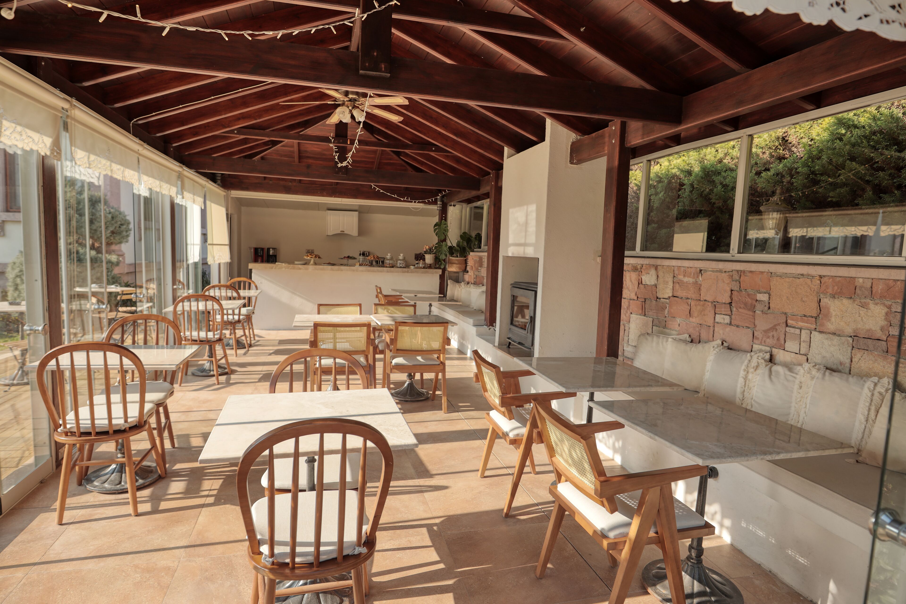 An outdoor patio with wooden tables and chairs, a brick wall, and a view of the kitchen area.