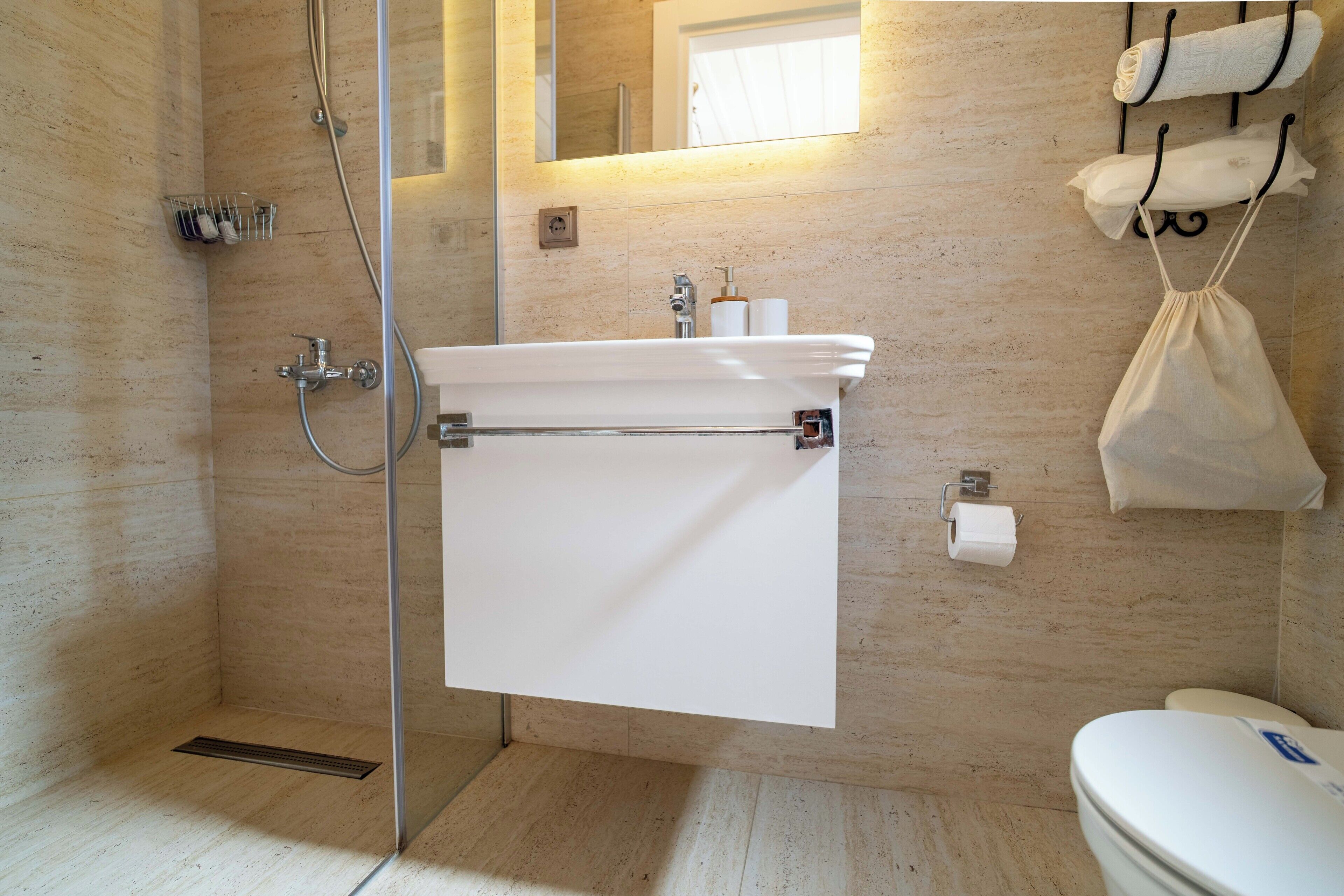 Een badkamer met een glazen douchecabine, een witte wastafel met een handdoekhouder erboven en een toilet met een keukenrolhouder.