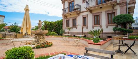 A courtyard with a fountain, outdoor seating, and a building with balconies.