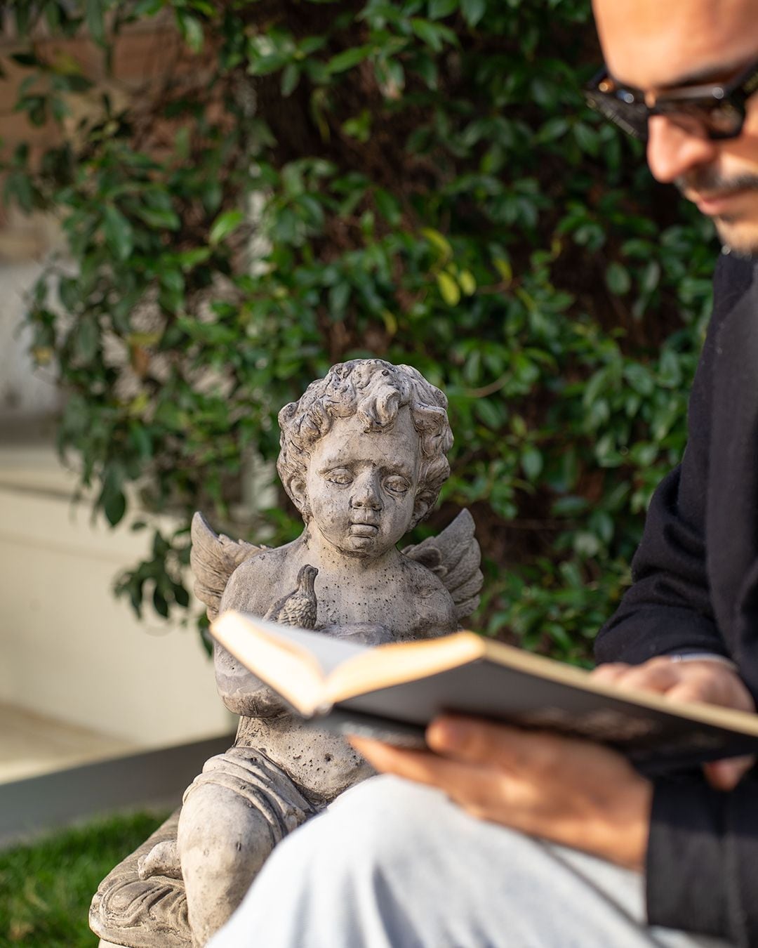 A person reading a book next to a stone statue of a child with wings.