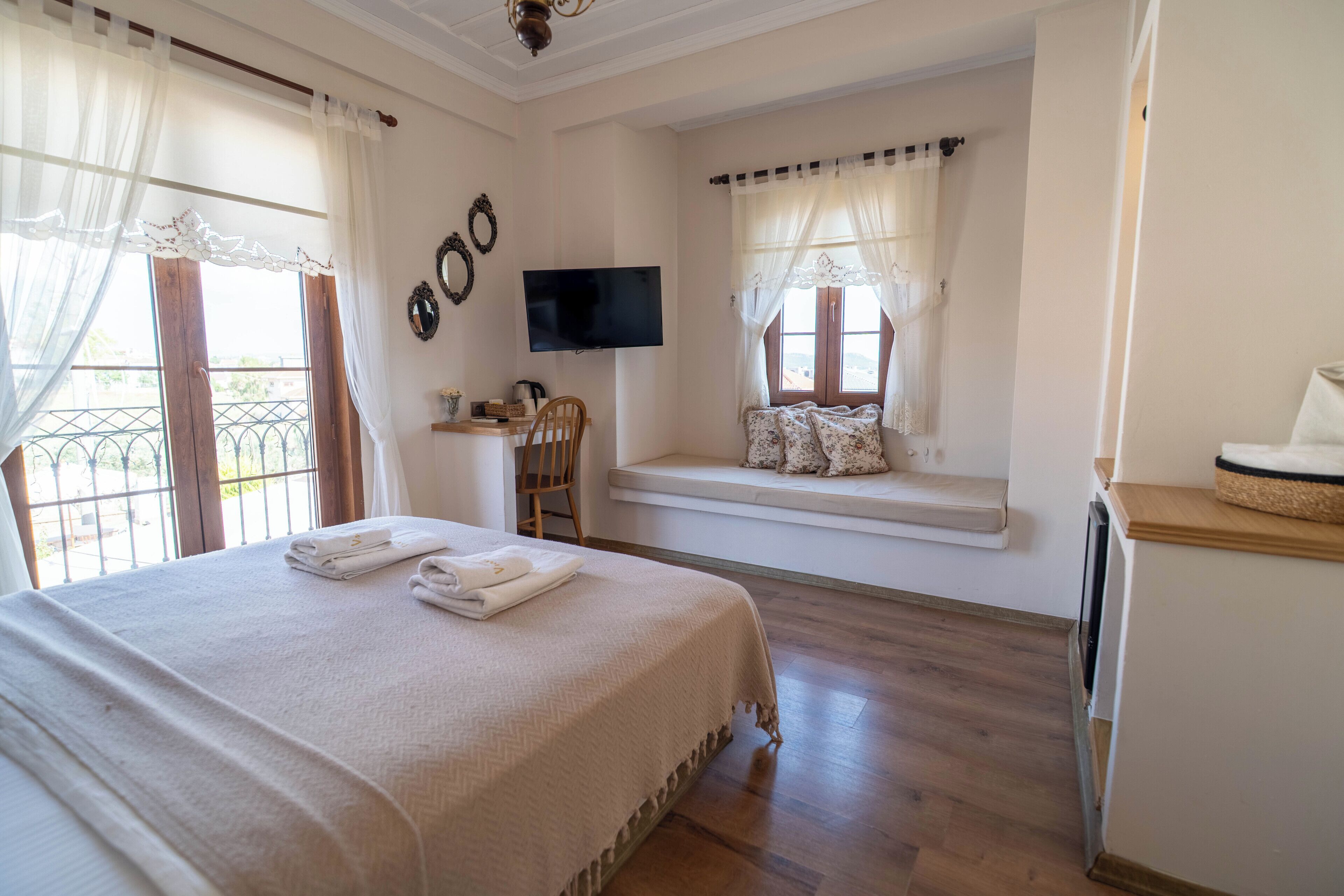 A hotel room with a bed, a TV, a window seat with cushions, and a view of the outdoors.