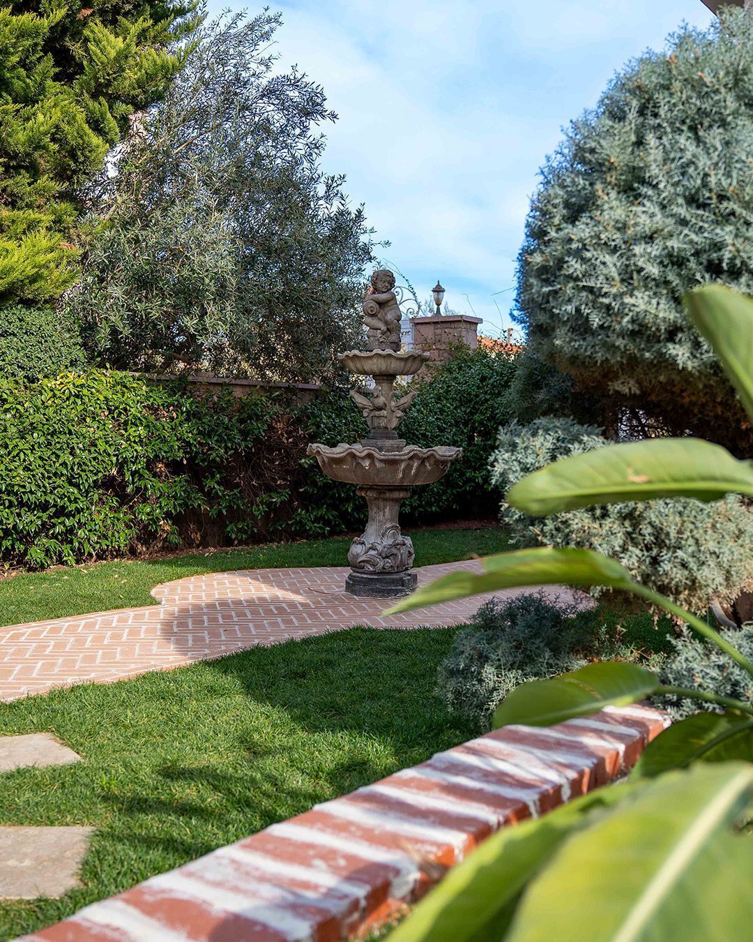 A garden with a stone fountain, a brick pathway, and lush greenery.