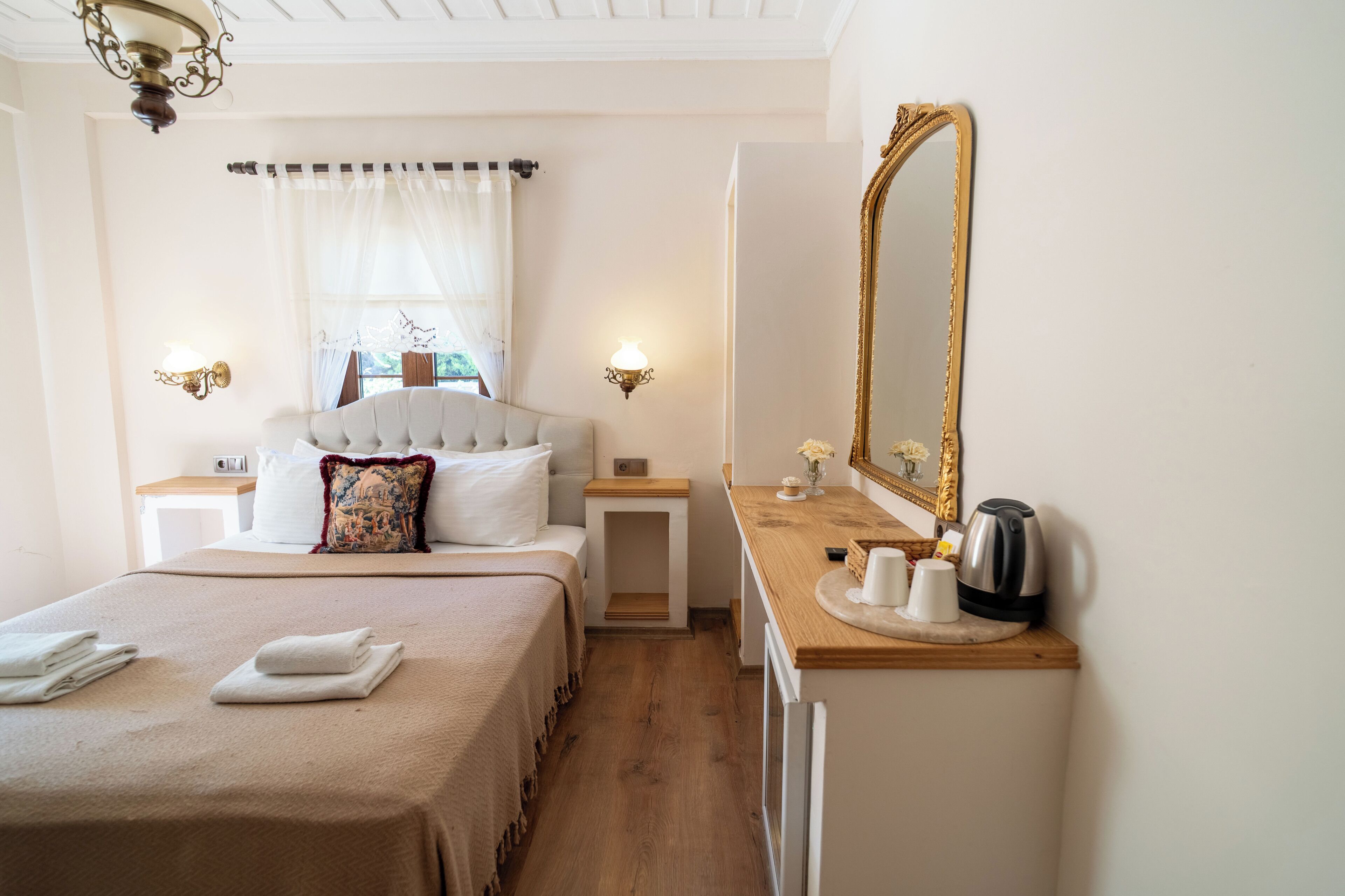 A hotel room with a bed, bedside tables, a vanity with a mirror, and a window with curtains.