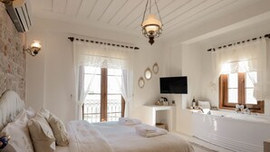 A bedroom with a large bed, a vanity with a mirror, a television, and a bathtub. - Cunda Vrodi By House (Ayvalik)