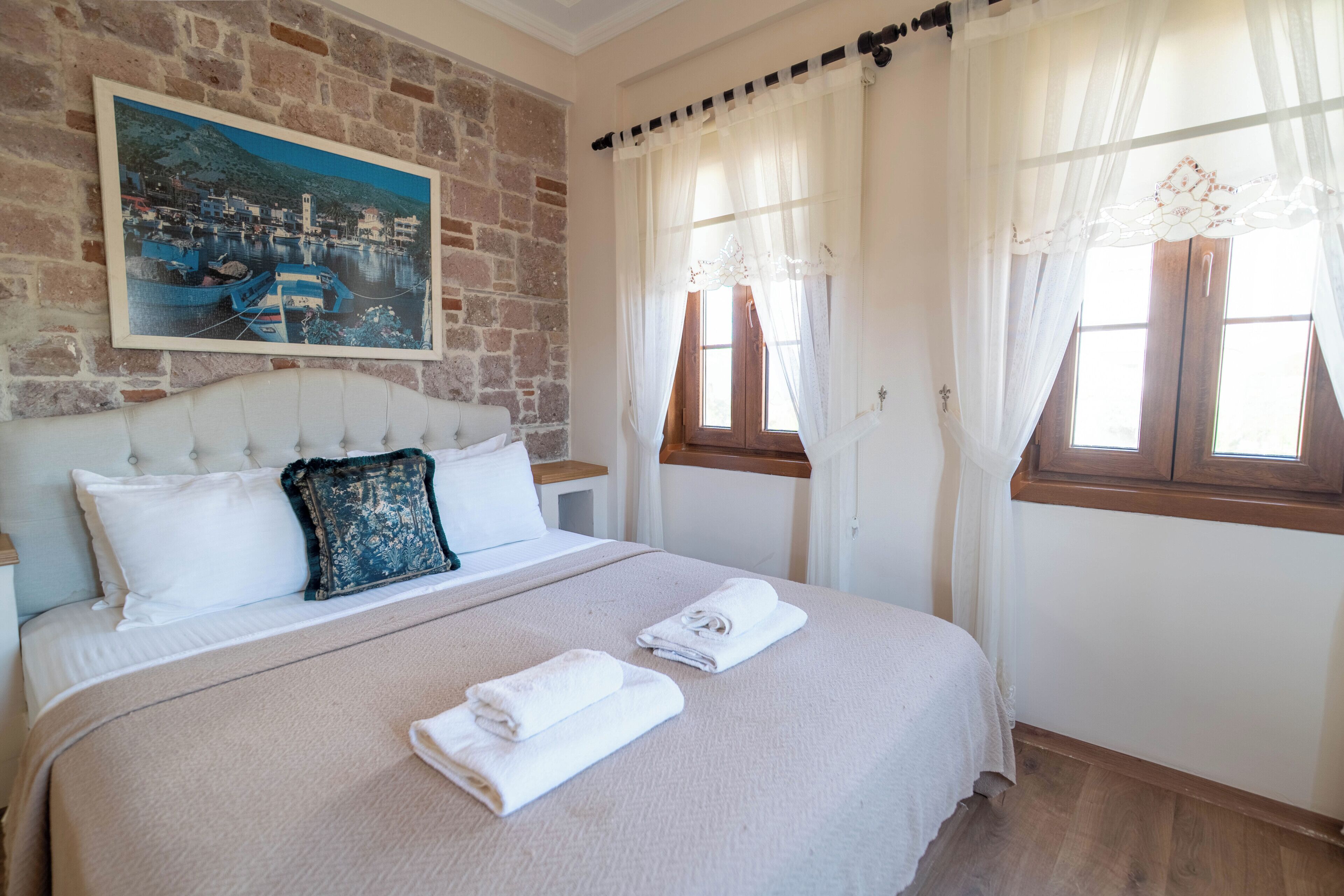 A bedroom with a bed, a painting on the wall, and a window with curtains.