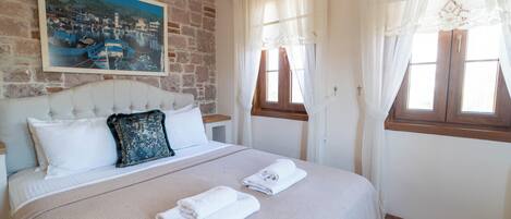 A bedroom with a bed, a painting on the wall, and a window with curtains.