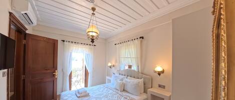 A hotel room with a large bed, a bedside table with a lamp, a small table with a vase and remote controls, and a large mirror.