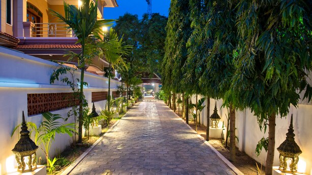 A paved pathway lined with trees and street lamps, leading to a building entrance. - Mei Mei Da Hotel (Siem Reap)