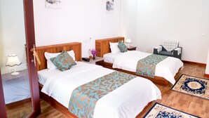 A hotel room with two beds, wooden headboards, white bedding, a nightstand with a lamp, and a small table with a chair. - Mei Mei Da Hotel (Siem Reap)