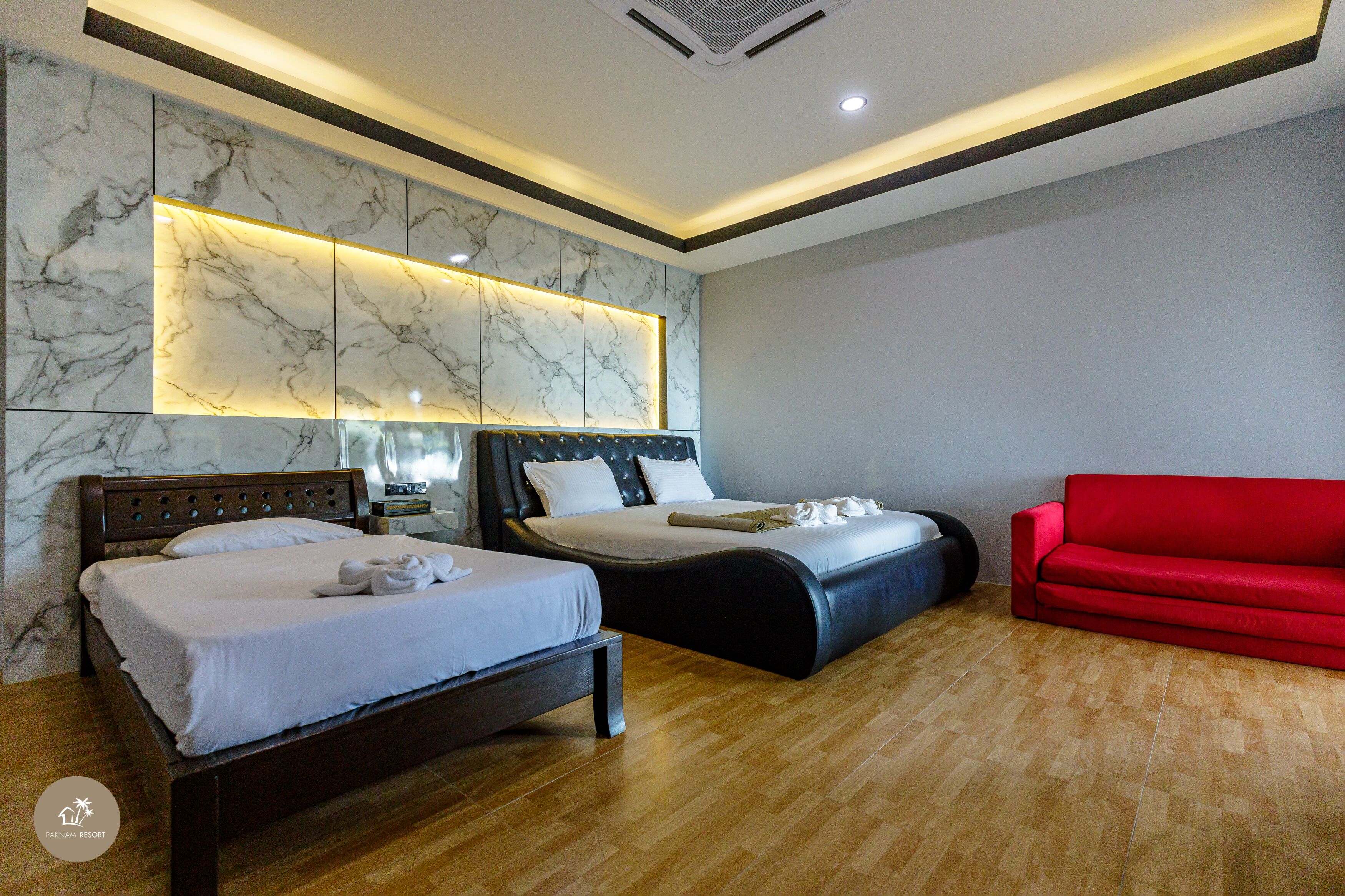 Habitación de hotel con dos camas, un sofá rojo, paneles de pared de mármol y suelo de madera.