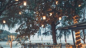 An outdoor seating area with tables and chairs, string lights, and a view of the sea. - Pak Nam Resort (La-ngu)