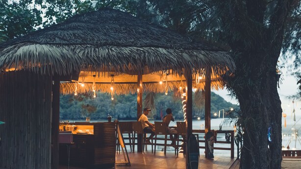 A thatched-roof outdoor dining area with wooden tables and chairs, overlooking a body of water. - Pak Nam Resort (La-ngu)