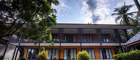Un bâtiment moderne à deux étages, doté d’une galerie couverte, entouré d’une végétation luxuriante et d’arbres à palmiers bien entretenus.