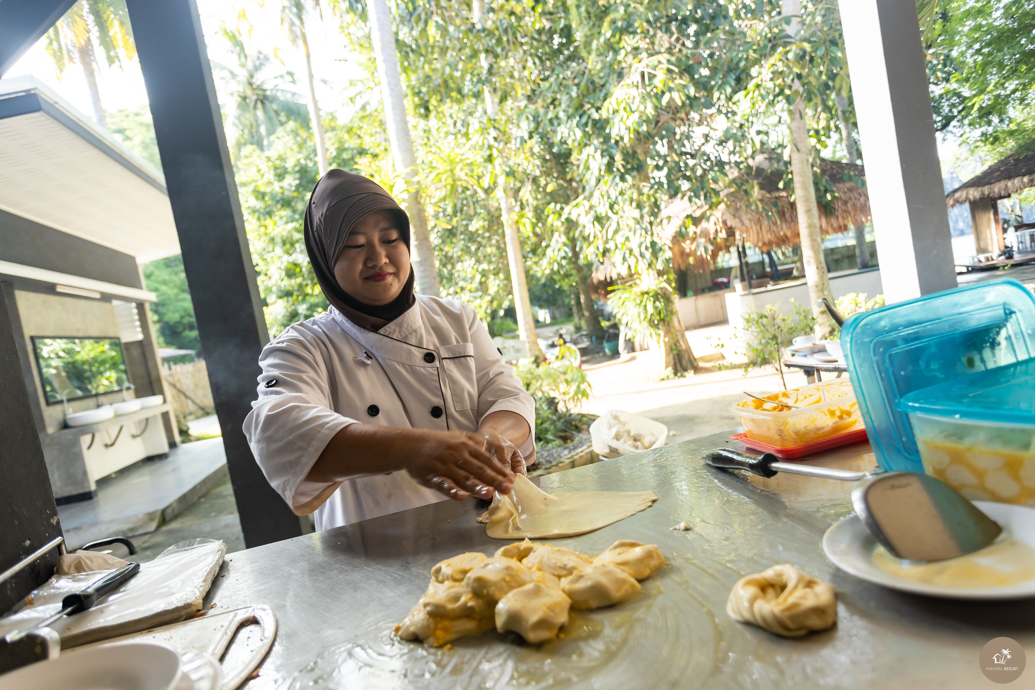 A chef preparing food outdoors with a table, cooking utensils, and ingredients visible.
