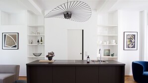 Una cocina moderna con una isla central, estantes blancos y una lámpara colgante.