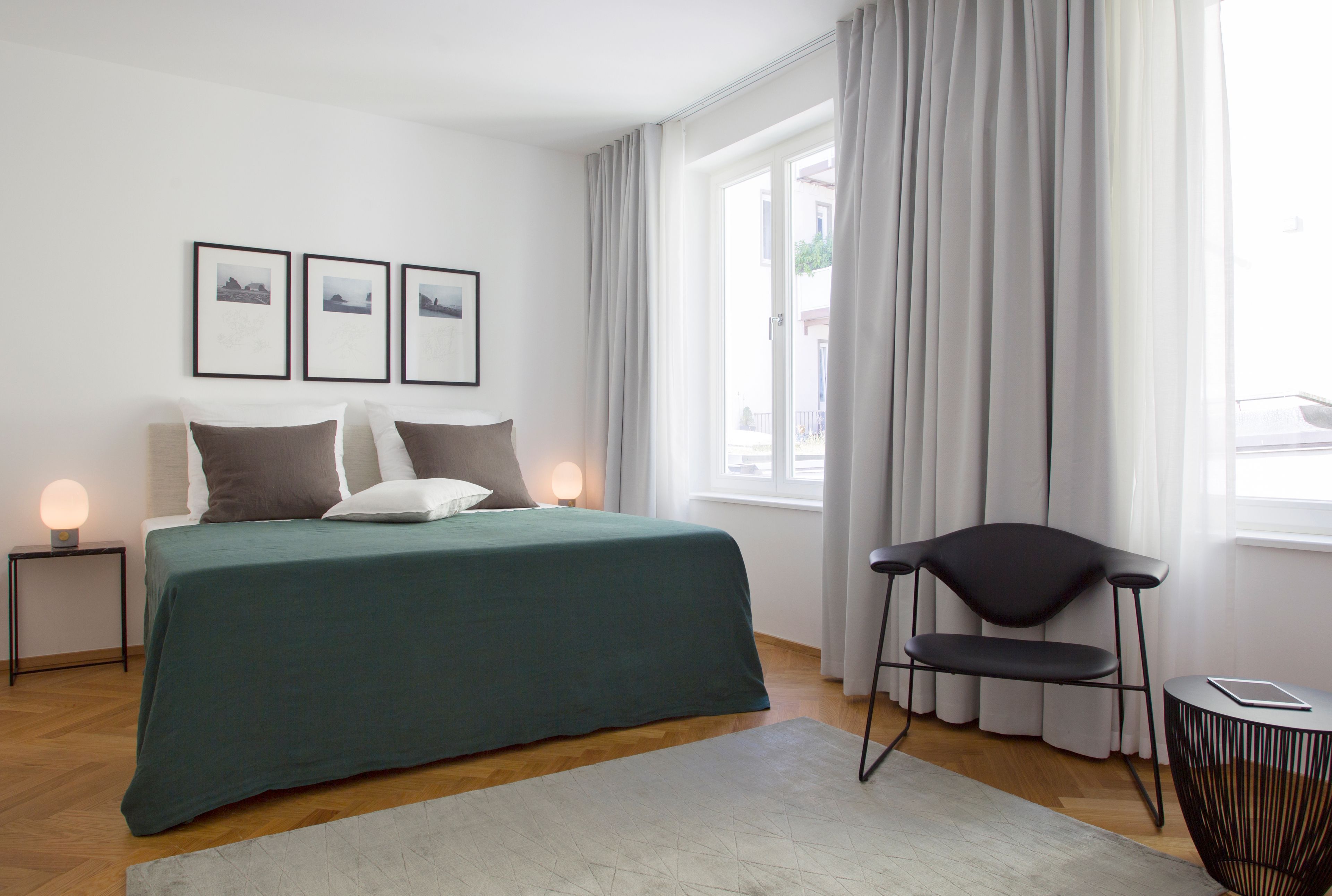 A modern bedroom with a bed, bedside lamps, a chair, and a window with curtains.
