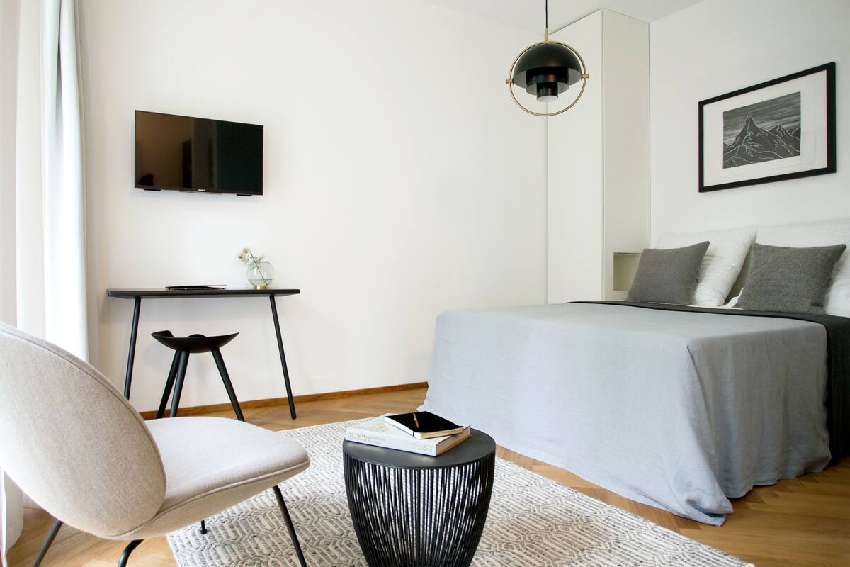 A modern bedroom with a bed, a desk, a chair, and a TV.