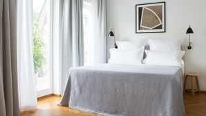 Una cama bien hecha con una colcha gris, dos lámparas de noche y una obra de arte abstracto enmarcada en la pared.