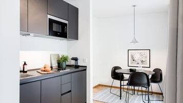 A modern kitchen with dark cabinets, a microwave, and a coffee machine. There is a dining area with a round table and black chairs.