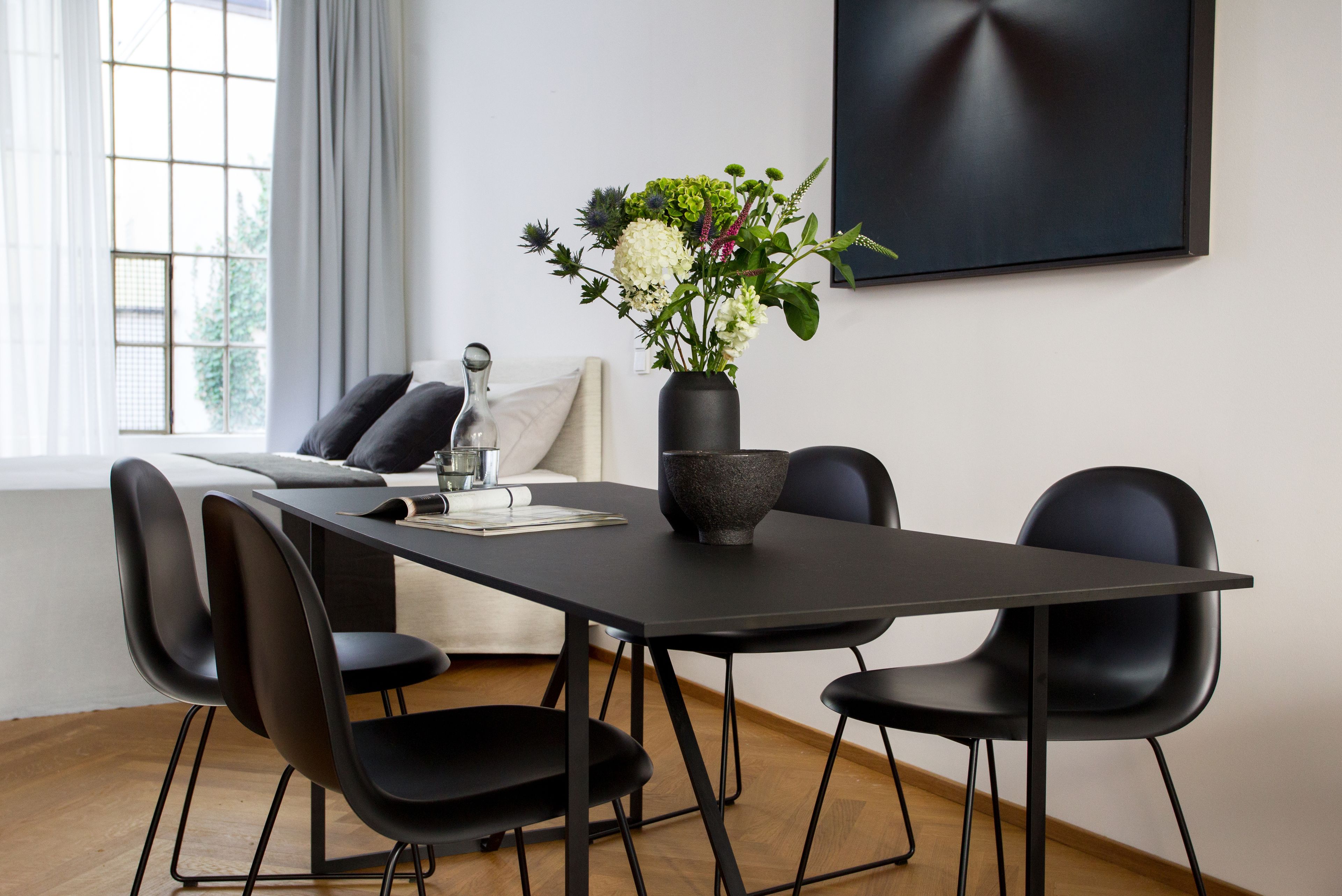 Ein moderner Essbereich mit einem schwarzen Tisch, vier schwarzen Stühlen, einer Vase mit Blumen und minimalistischer Einrichtung.