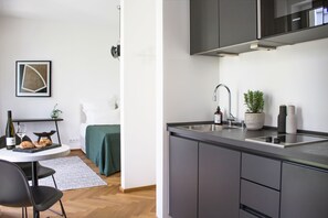 A modern kitchen with grey cabinets, a stainless steel sink, and a built-in oven. There is a small dining area with a table and chairs, and a potted plant on the counter. - August The Boardinghouse (Hamburg)
