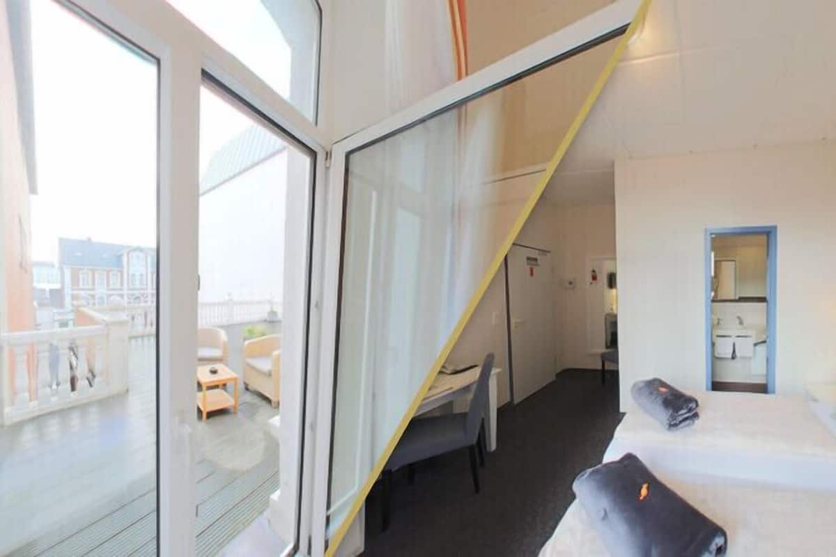 Quarto de hotel com varanda, uma cama, uma escrivaninha e um banheiro visível através de uma porta aberta.