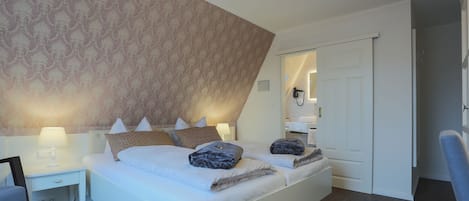 Una habitación de hotel moderna con una cama grande, mesitas de noche con lámparas y un papel tapiz estampado.