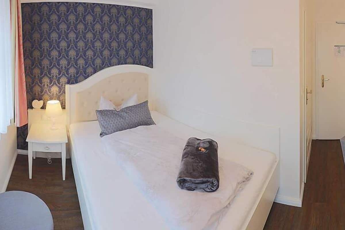 Quarto de hotel com cama, mesa de cabeceira, abajur e escrivaninha com cadeira.