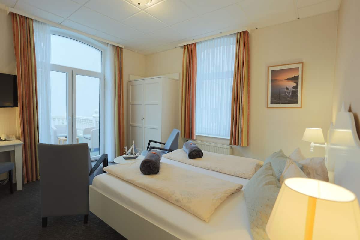 Quarto de hotel com cama, escrivaninha, cadeira, televisão e janela com cortinas.