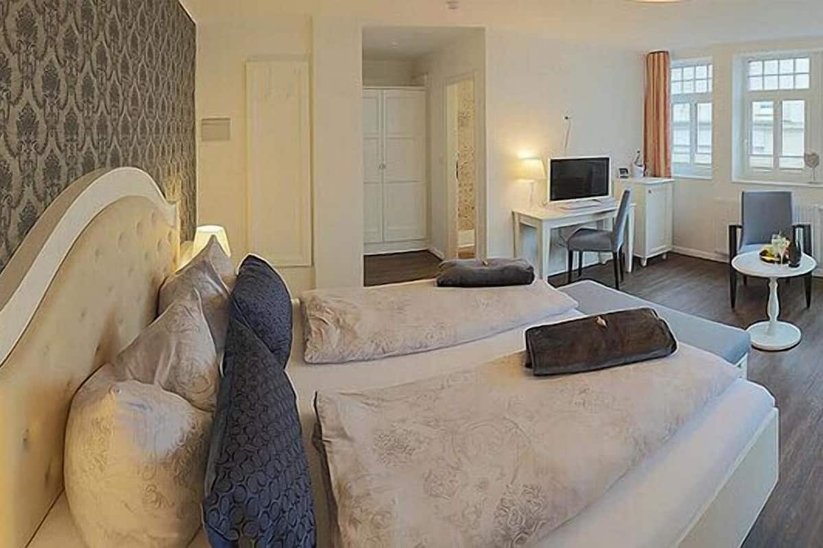 Quarto de hotel com cama, escrivaninha com computador, mesinha com bebida e sofá.