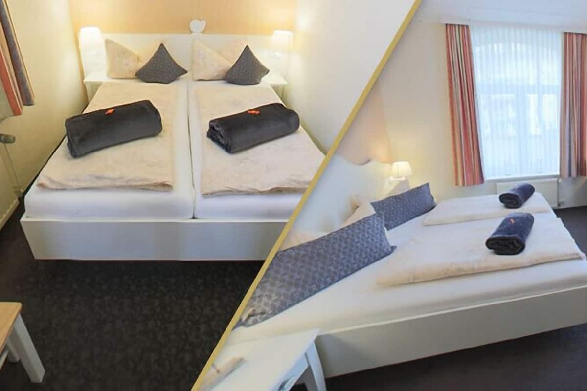 Quarto de hotel com cama, escrivaninha, cadeira e televisão.