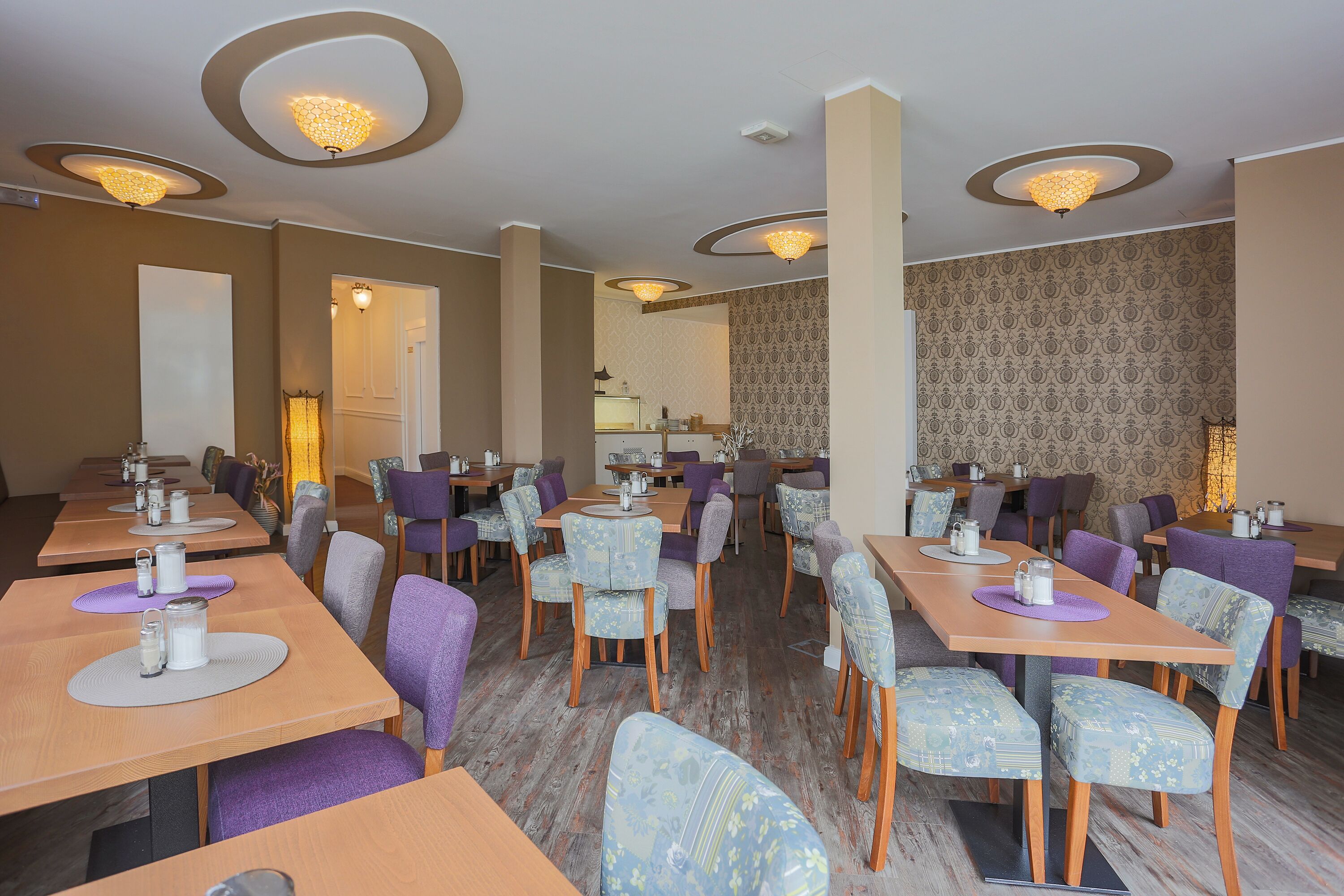 Ein Restaurant mit mehreren Tischen und Stühlen, das ein modernes Design mit gemustertem Wandpapier und Deckenleuchten aufweist.