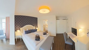 A modern hotel room with a large bed, a desk, and a view of the city through large windows. - Hotel Strandvilla Janine (Borkum)