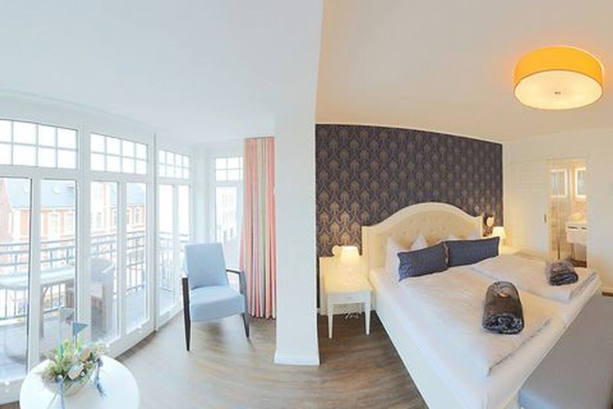 Quarto de hotel moderno com uma cama grande, uma escrivaninha e vista para a cidade através de amplas janelas.