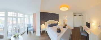 A modern hotel room with a large bed, a desk, and a view of the city through large windows.