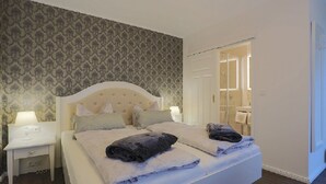 A neatly made bed with pillows and a blanket, a bedside table with a lamp, and a patterned wallpaper on the wall. - Hotel Strandvilla Janine (Borkum)