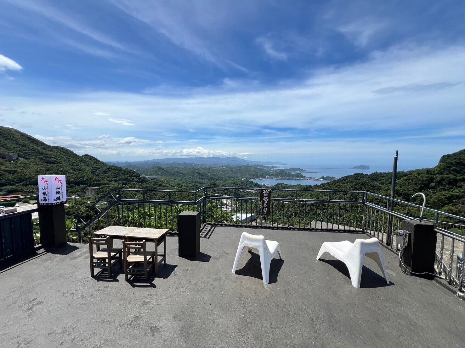 Una terraza con mesa y sillas, barandilla y una vista panorámica del paisaje costero.
