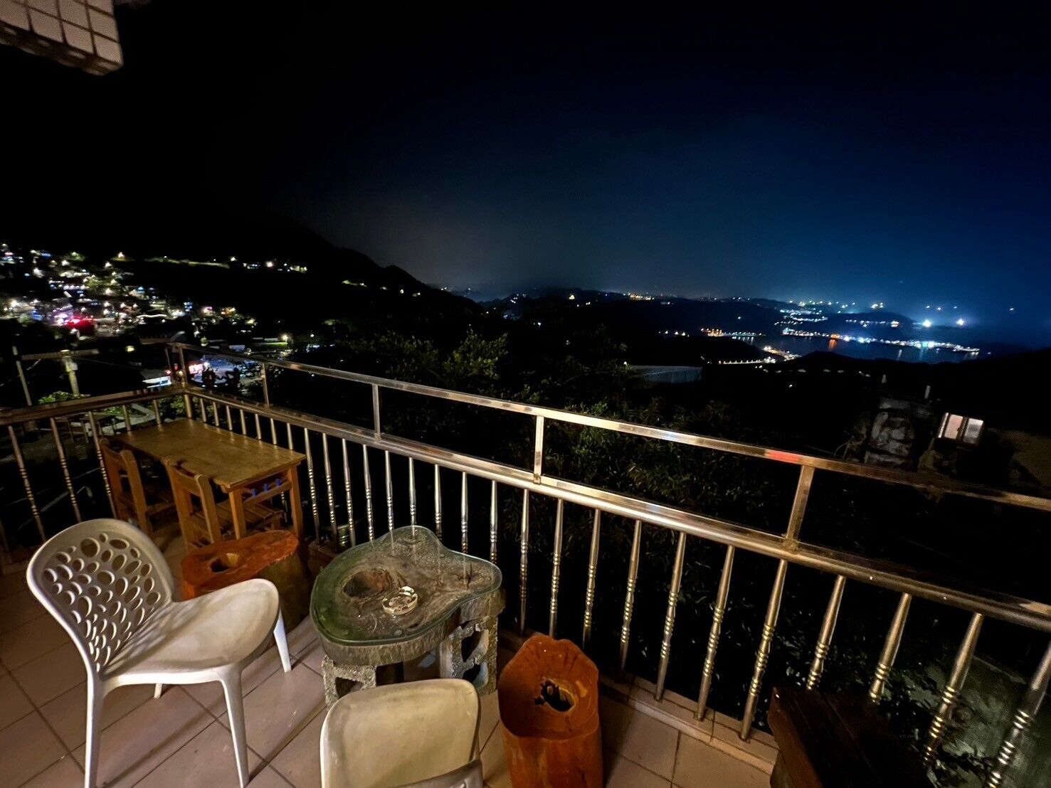 Un balcone con tavolo e sedie, affaccia su una vista notturna della città.