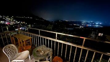 Un balcone con tavolo e sedie, affaccia su una vista notturna della città.