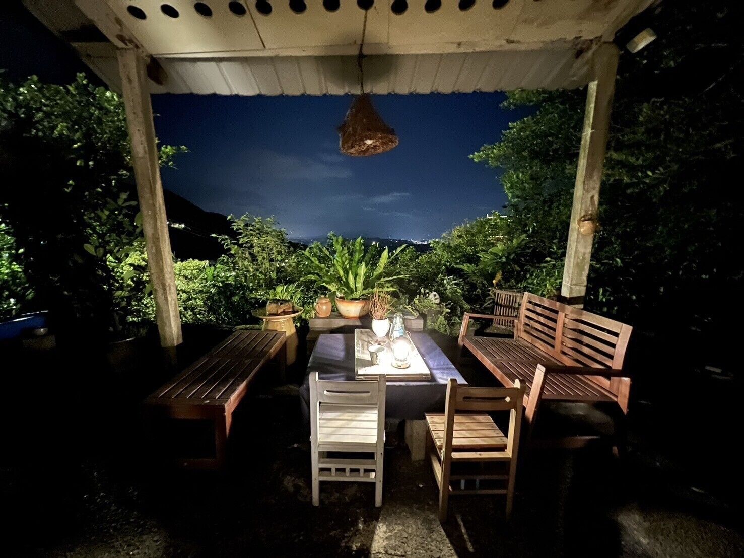An outdoor patio with wooden furniture, potted plants, and a hanging light fixture.