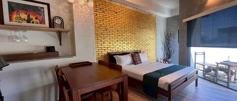 A room with a brick wall, a bed, a dining table, and a balcony with chairs.
