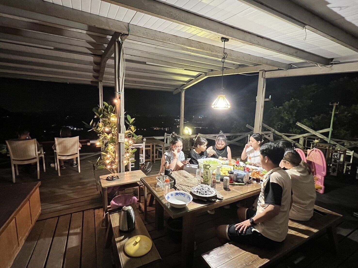 Un grupo de personas cenando en una mesa al aire libre bajo una cubierta, con vista al cielo nocturno.