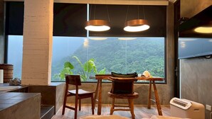 Ein Schlafzimmer mit einem Bett, einem Schreibtisch, zwei Stühlen, einem Tisch und einem Fenster mit Blick auf einen bewaldeten Bereich.
