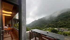 Ein Balkon mit Tisch und Stühlen, eine hölzerne Bank und Blick auf eine gebirgige Landschaft.