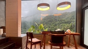 Ein Zimmer mit großem Fenster, Holzstühlen, einem kleinen Tisch und einer Treppe.